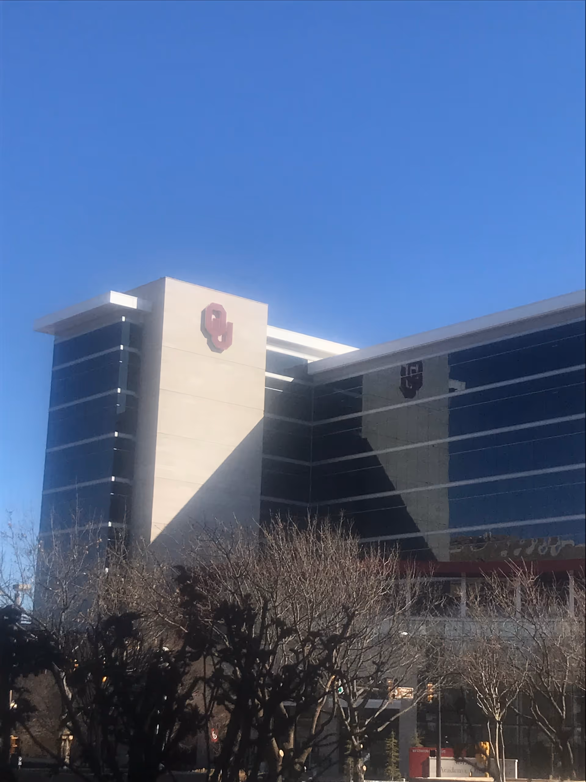 Modern clinic building with glass facade, beige tower, and red emblem against blue sky.