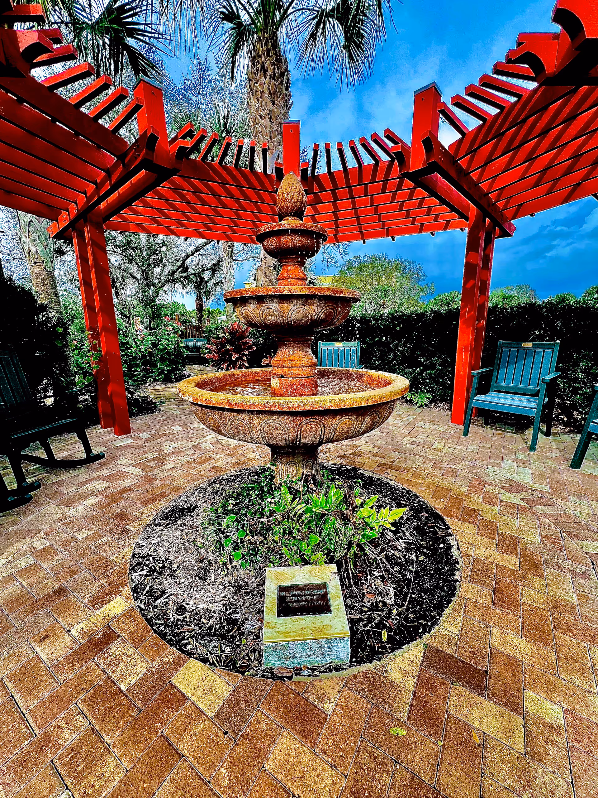 A stone fountain under a red pergola on a brick-paved outdoor garden patio.