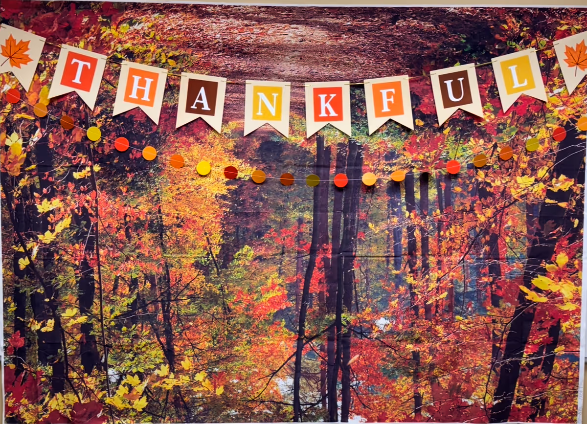 Autumn forest backdrop with a colorful THANKFUL banner hung indoors.