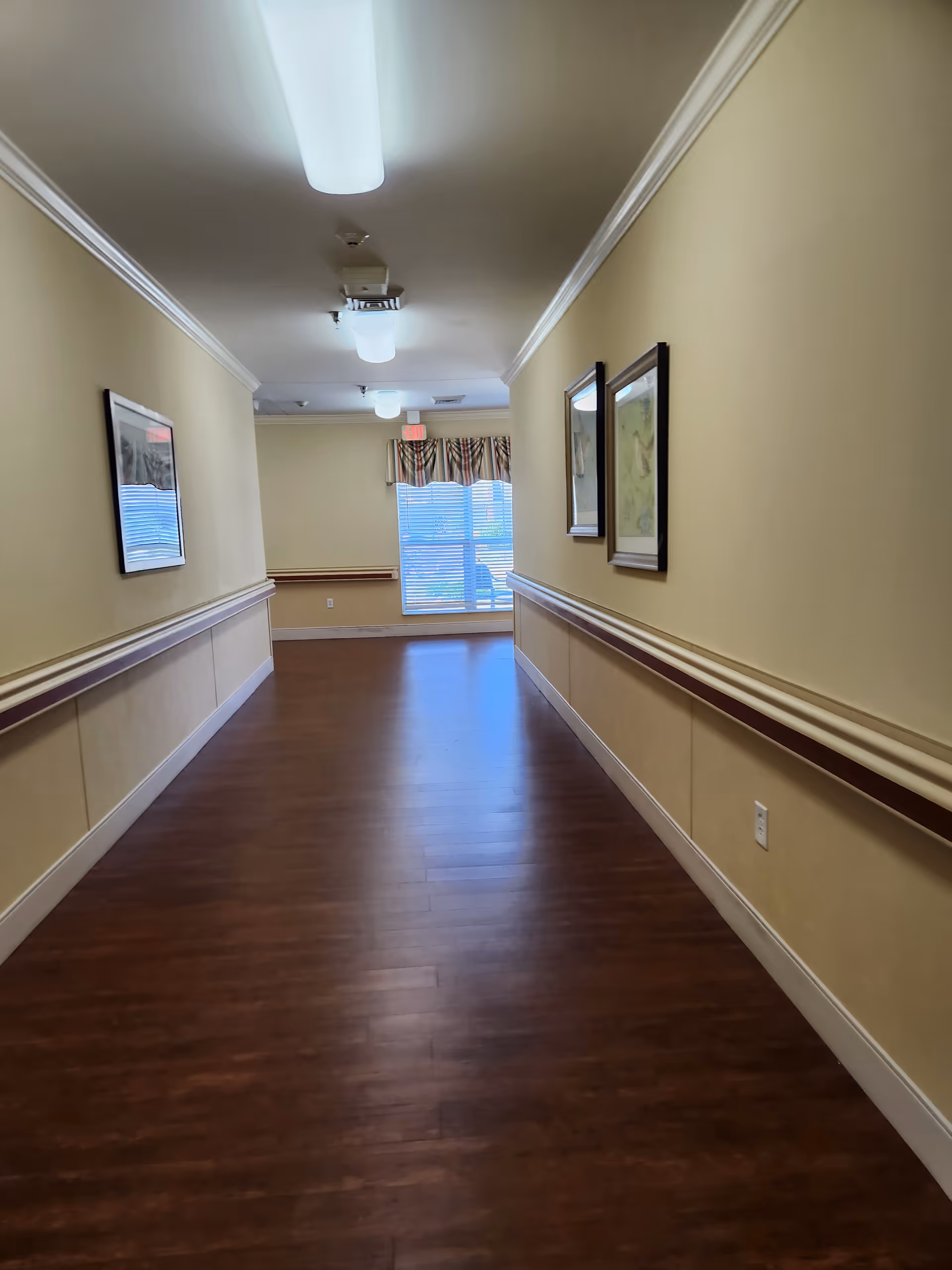 Long hallway inside a senior living facility with wood floors and wall art.