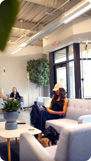 Resident sits on a gray sofa in a modern clinic lounge using a smartphone.