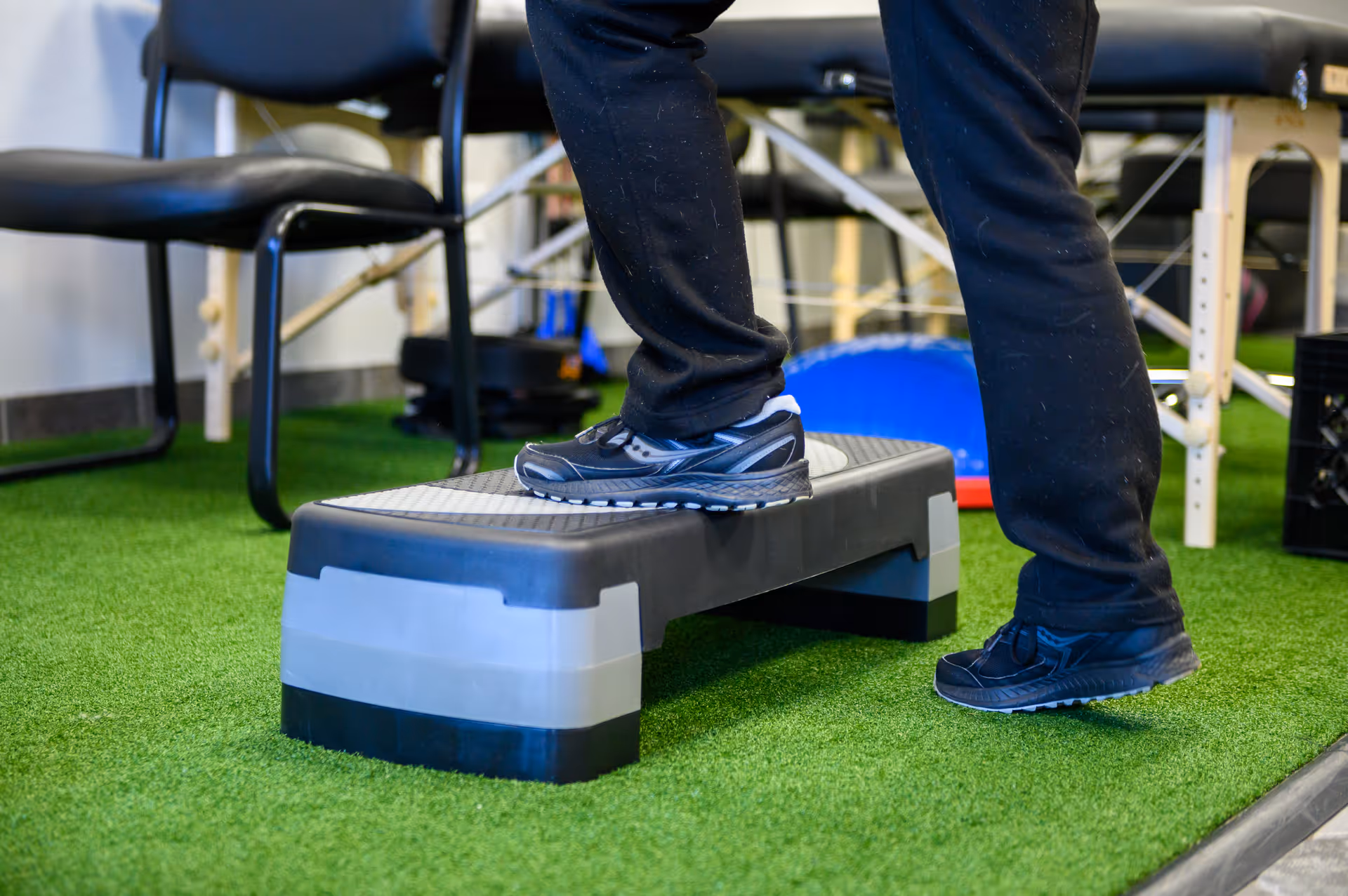 Close-up of a person stepping onto a gray step platform on artificial turf in therapy room.