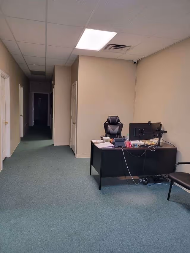 Desk with computer and chair beside a long hallway in a beige interior.