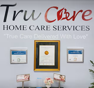 Wall displays TruCare Home Care Services sign with framed certificates and flowers.