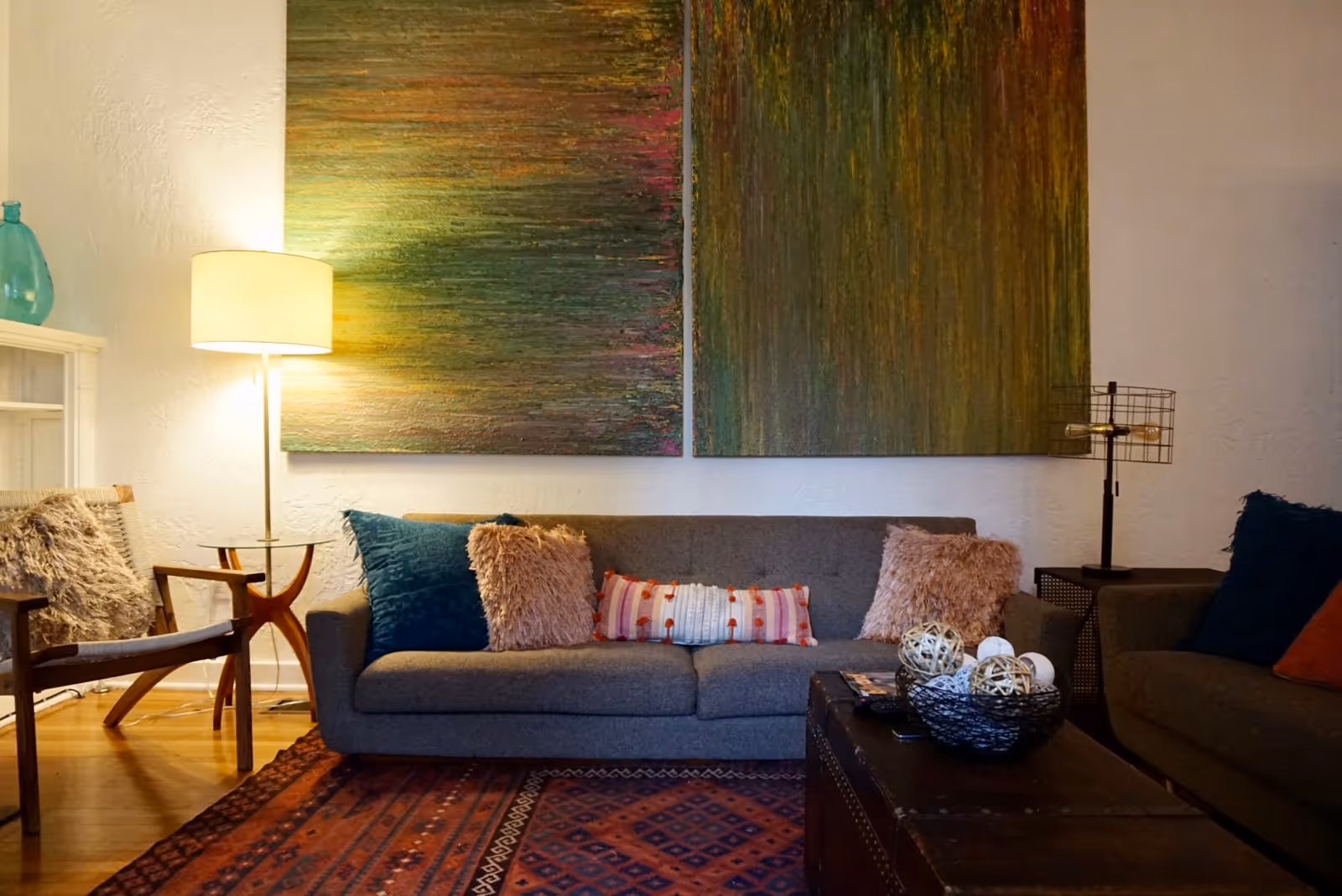 Cozy living room with a gray sofa, colorful cushions, two abstract paintings, a floor lamp, rug.
