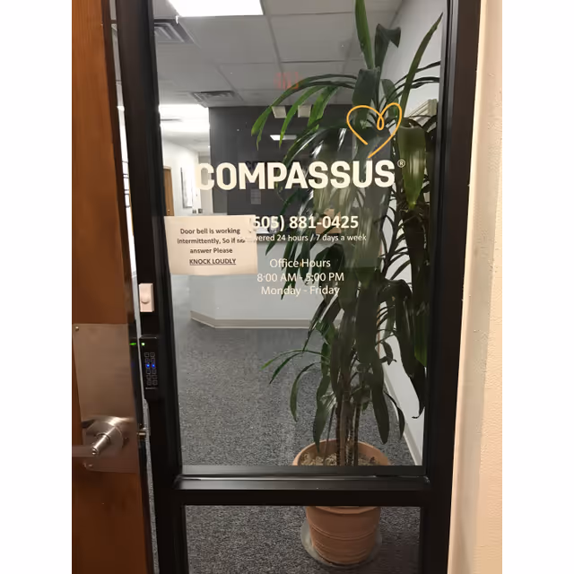 Glass door with Compassus Home Health sign and a potted plant inside a hallway