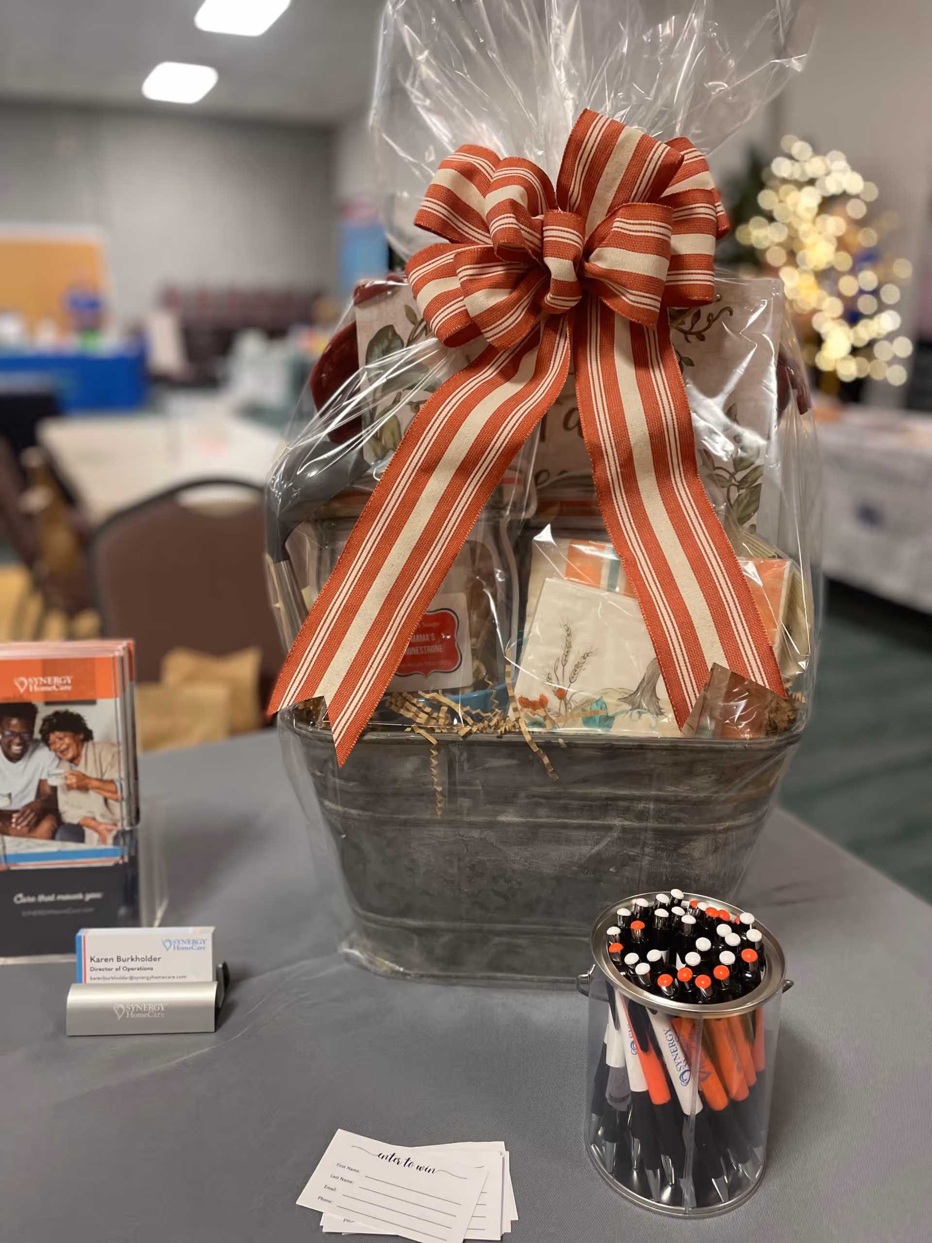 Gift basket wrapped in cellophane with a red bow sits on a gray indoor table.