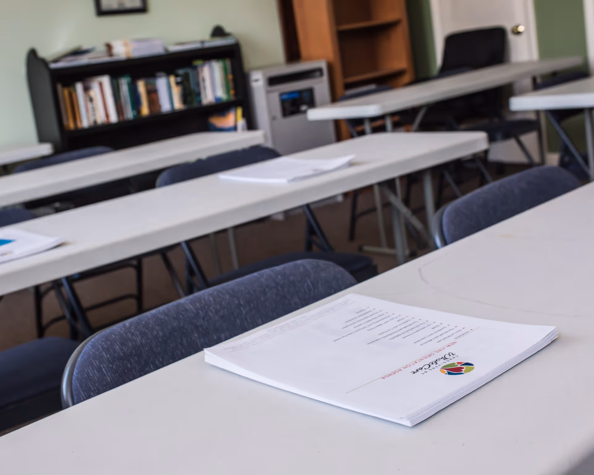 Indoor classroom-style room with long tables, chairs, and scattered papers.