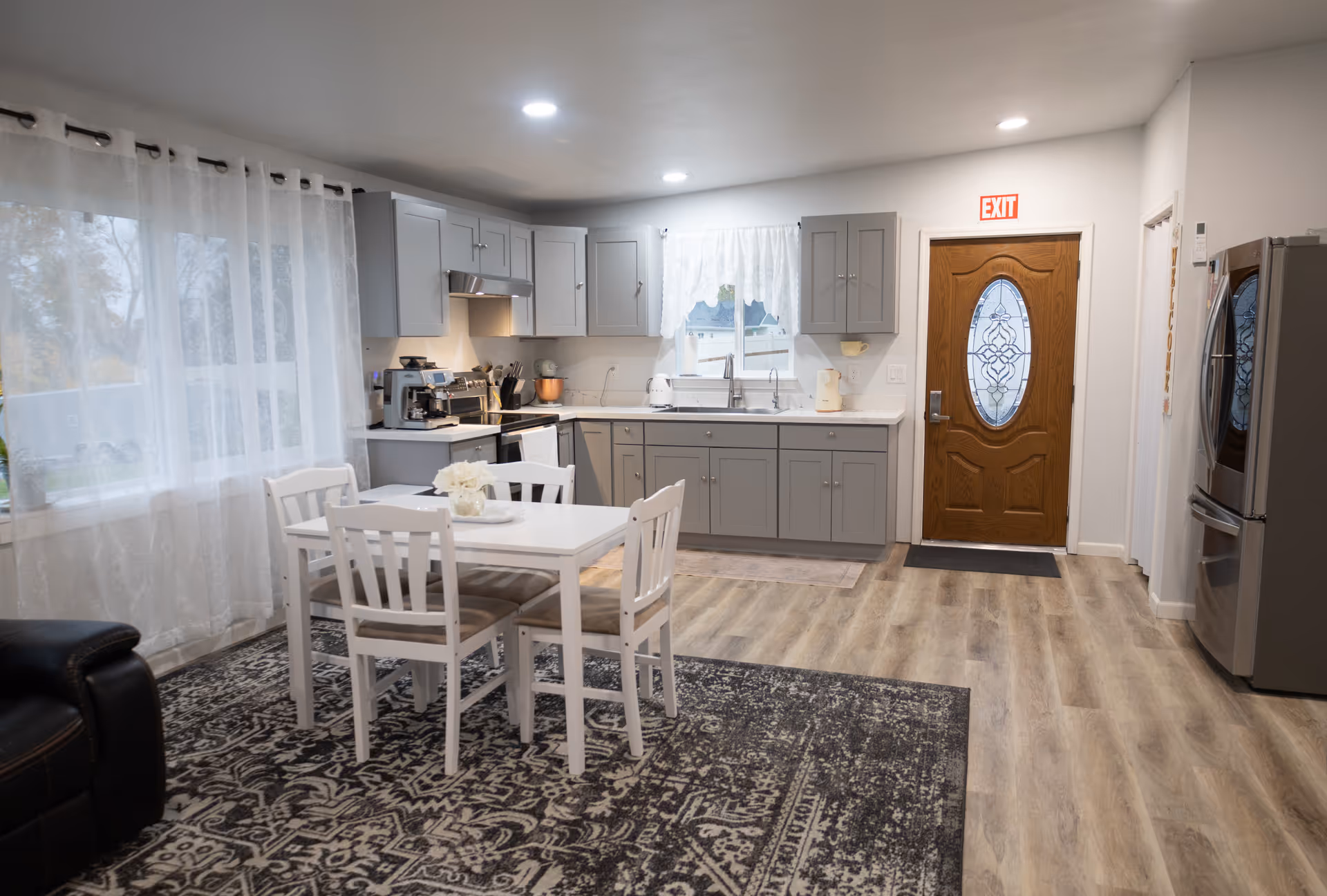 Bright open kitchen and dining area with gray cabinets, white table, and patterned rug.