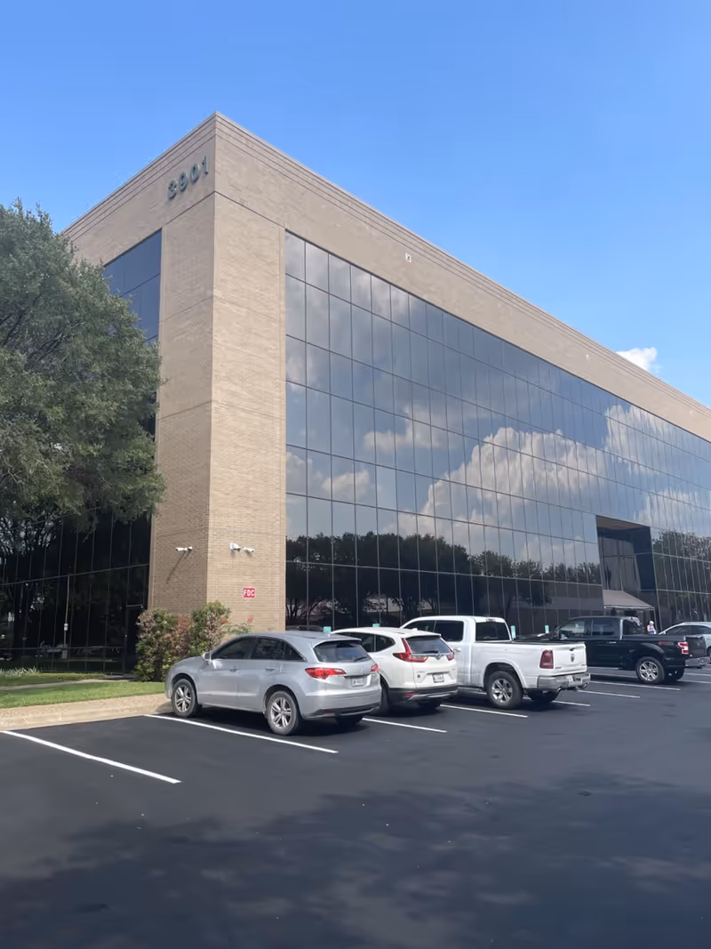 Glass-clad office building with a large parking lot and blue sky reflection.