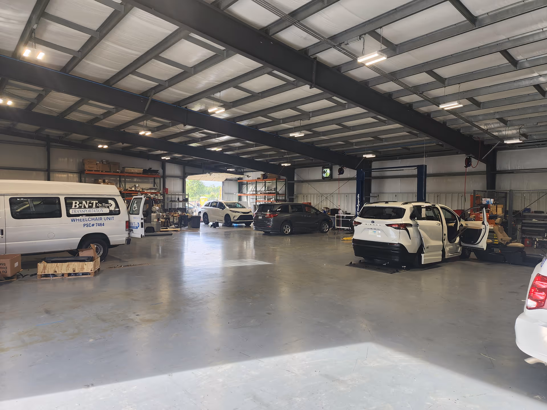 Indoor automotive workshop with multiple cars and equipment in a spacious warehouse.