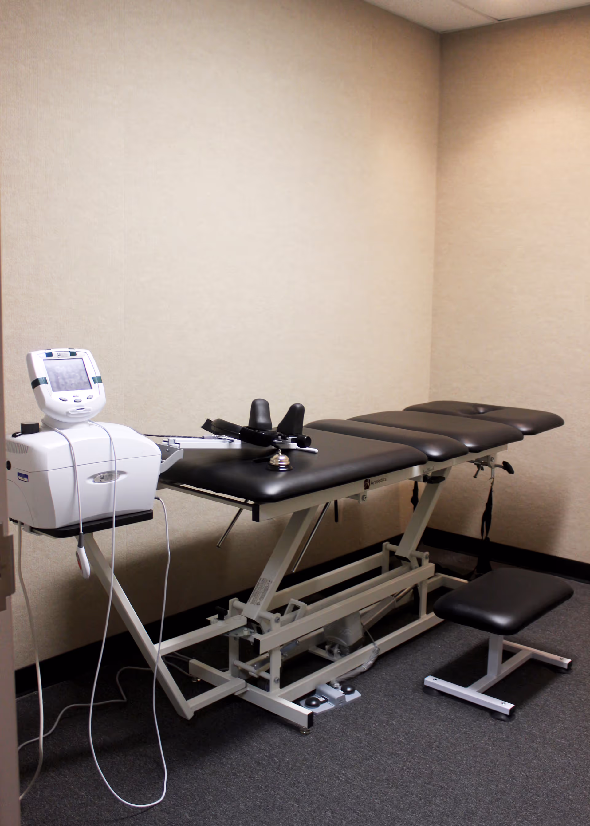 A medical therapy table with equipment in a small beige treatment room at a senior facility.
