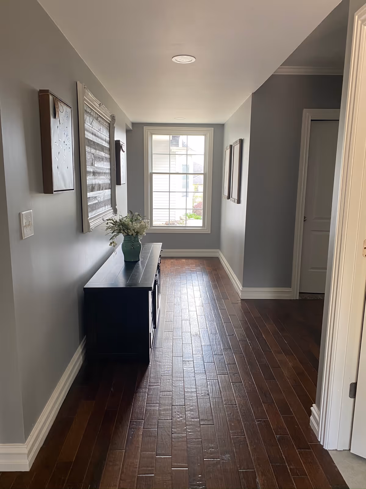Hallway interior at Addison-Oaks Manor with dark wood floors, wall art, and a console table.