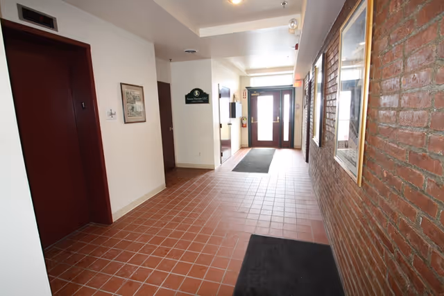 Indoor corridor in a senior living facility with brick wall, tile floor, and glass doors.