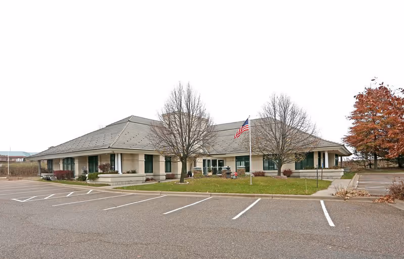 Front view of a single-story senior living facility with parking and flag.
