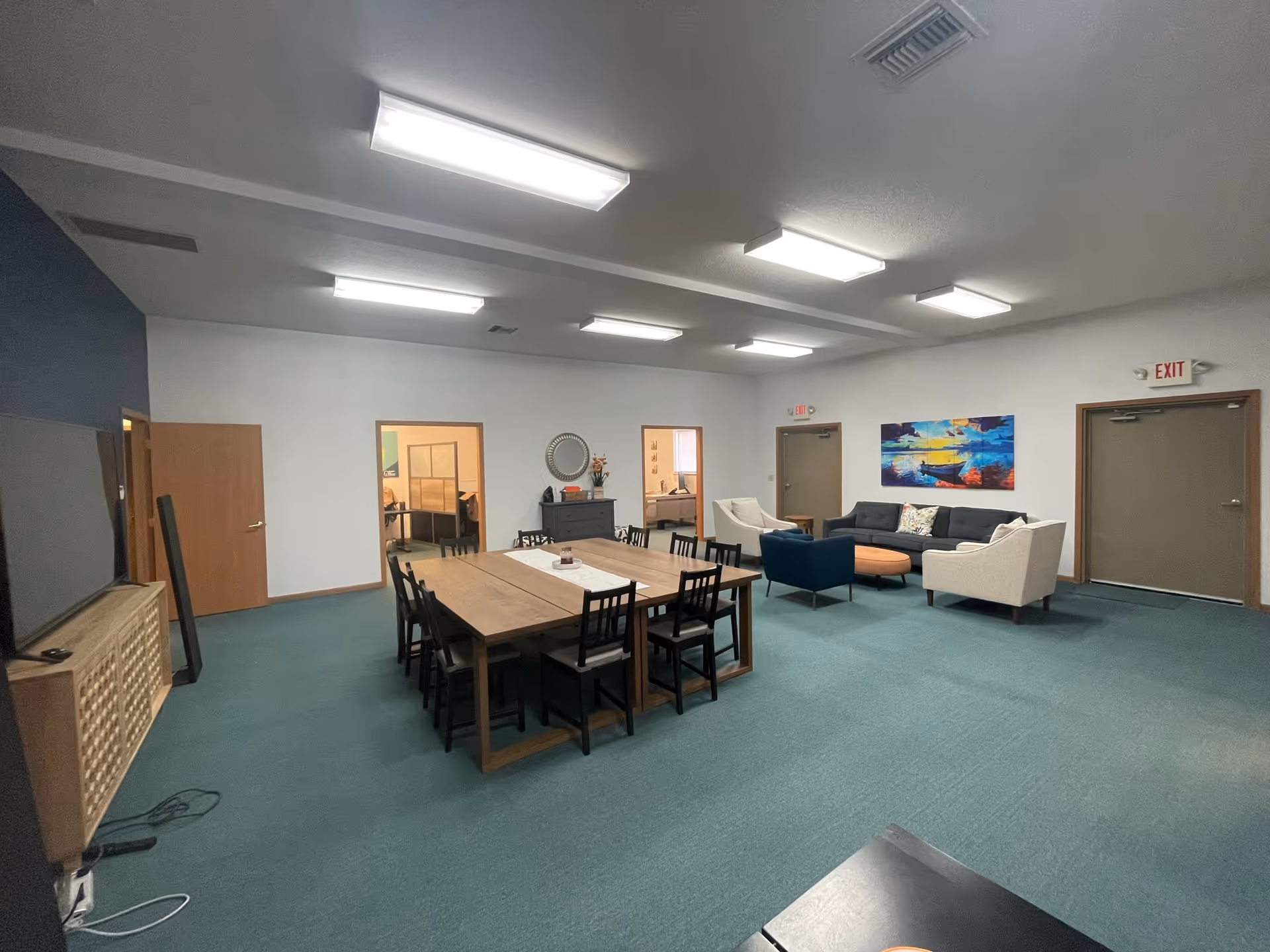A large community room with a long dining table, chairs, and a seating area.