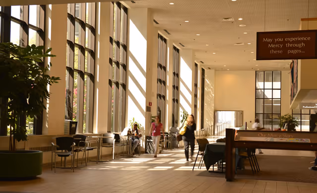 Bright Mercy facility lobby with tall windows, seating along the wall, and a few visitors.
