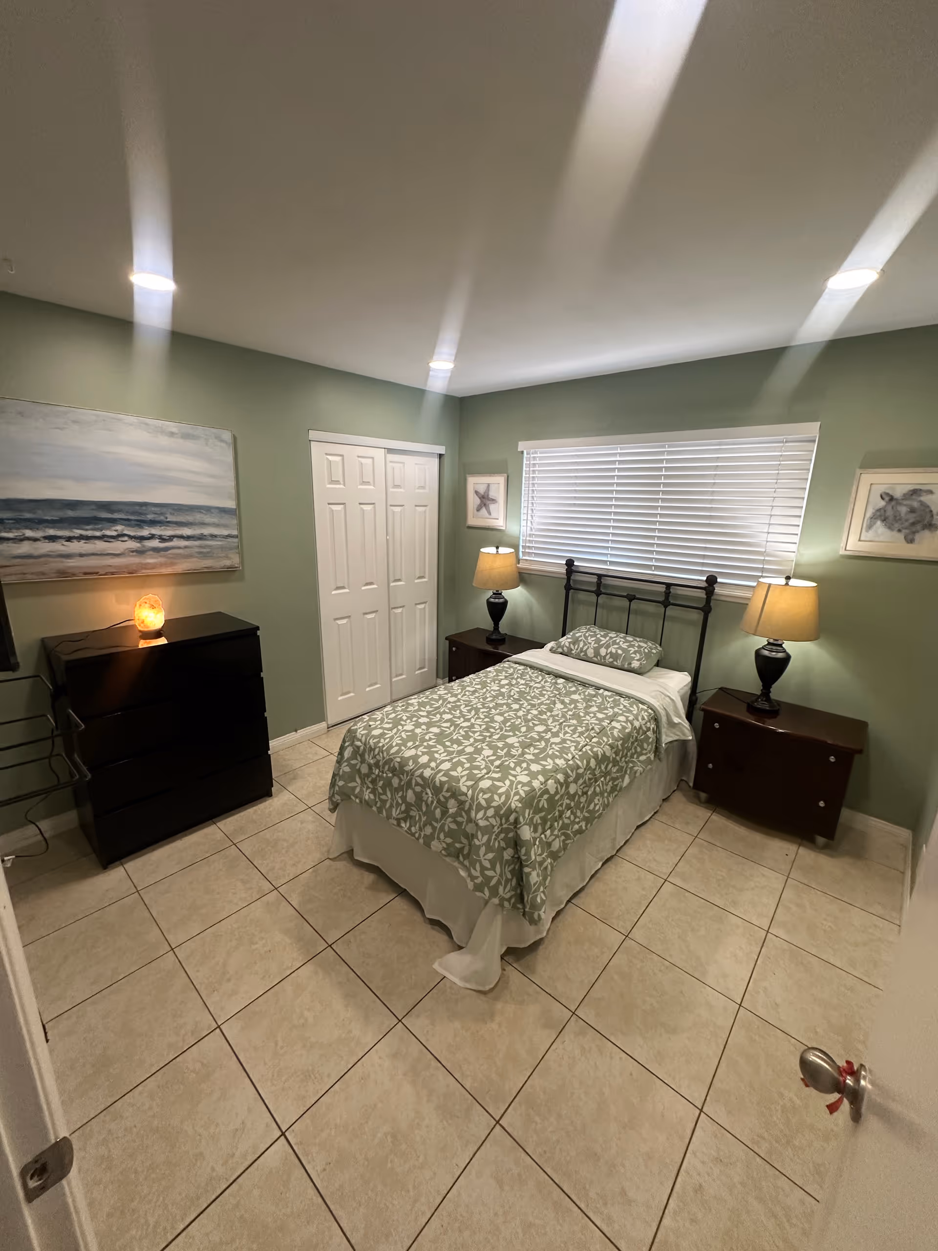 A neatly made bedroom with a metal bed, green walls, and lamps.