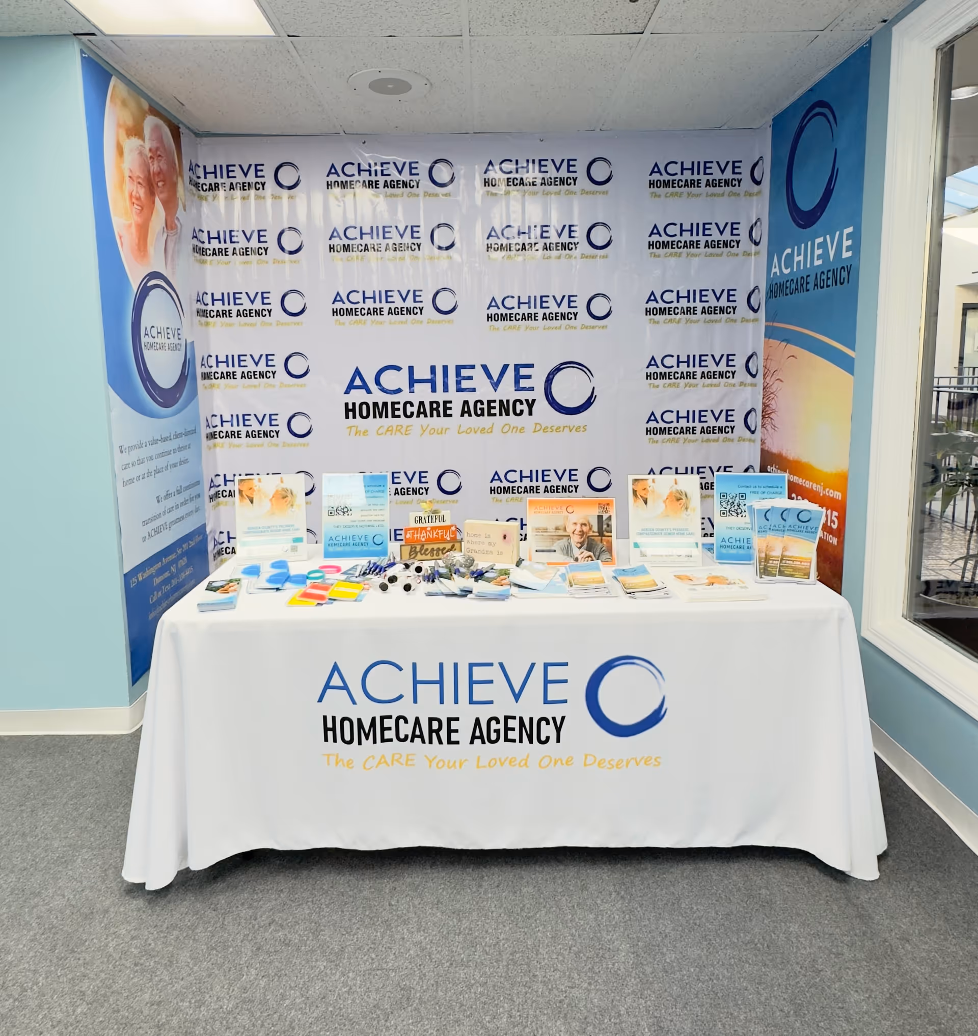Promotion table with brochures against a backdrop branded with Achieve Homecare Agency logos.