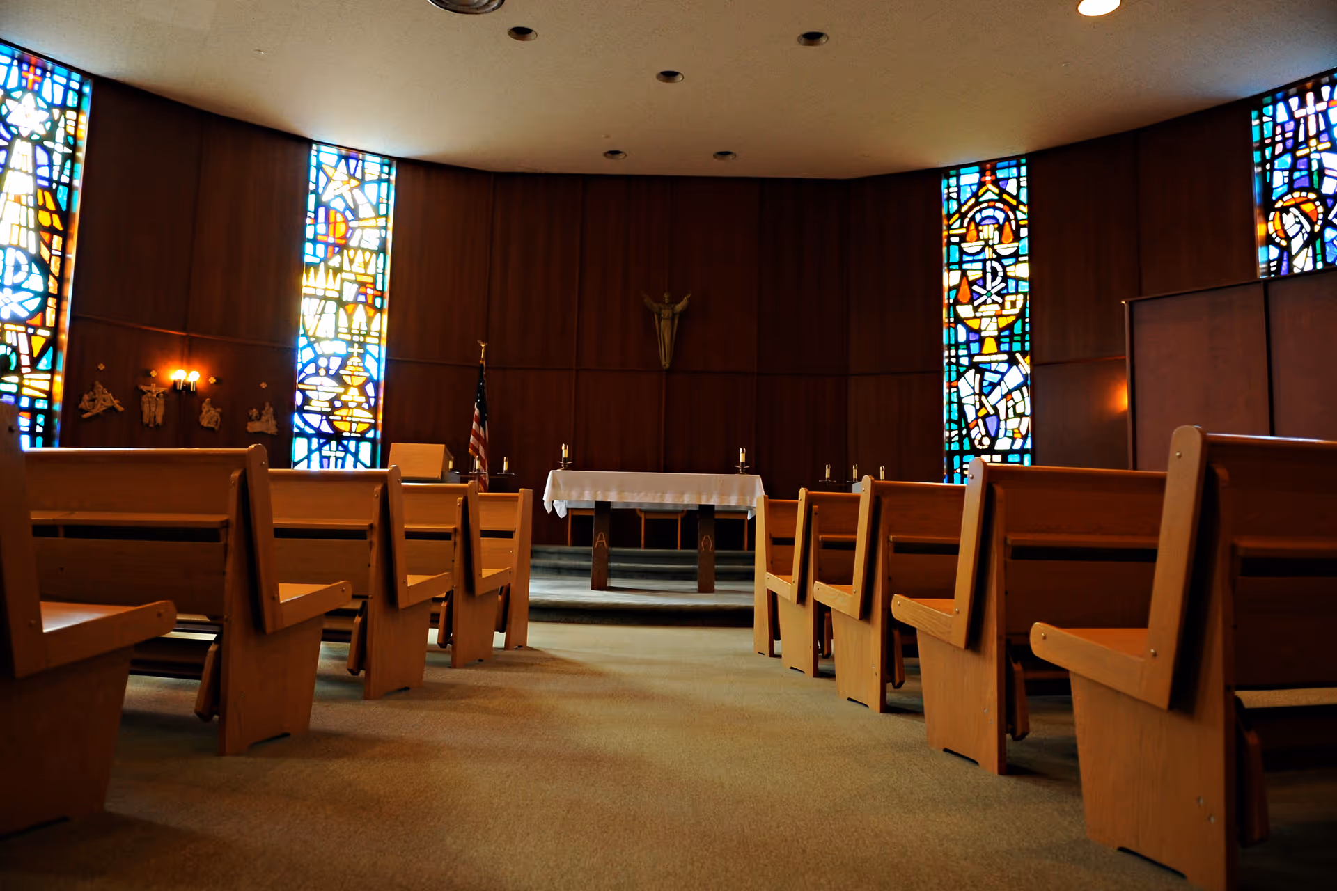 Empty chapel inside a hospital with wooden pews, stained glass, and an altar.