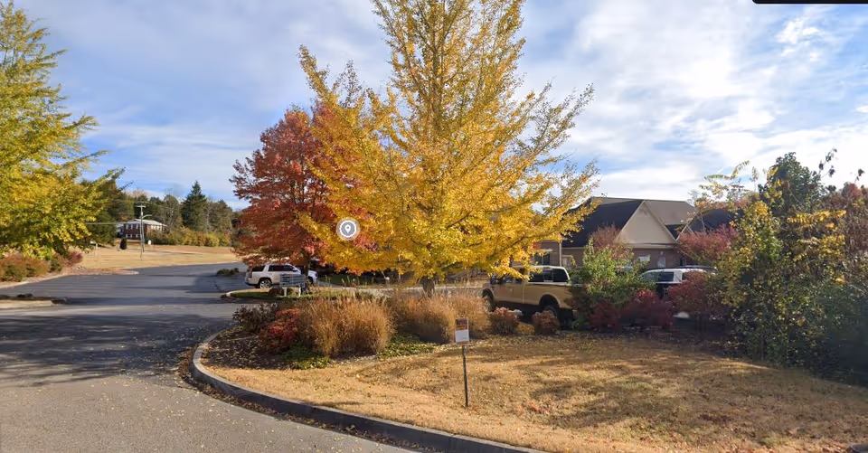Campus entrance with autumn trees, a curved driveway, and parked vehicles near a building.