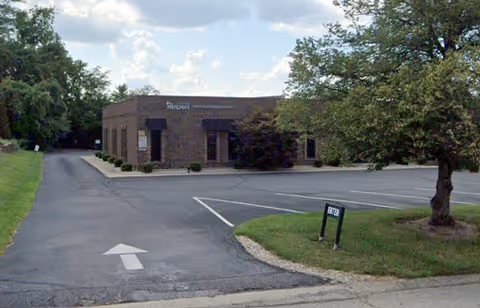 Front exterior of a brick Senior Helpers facility with parking lot and trees.