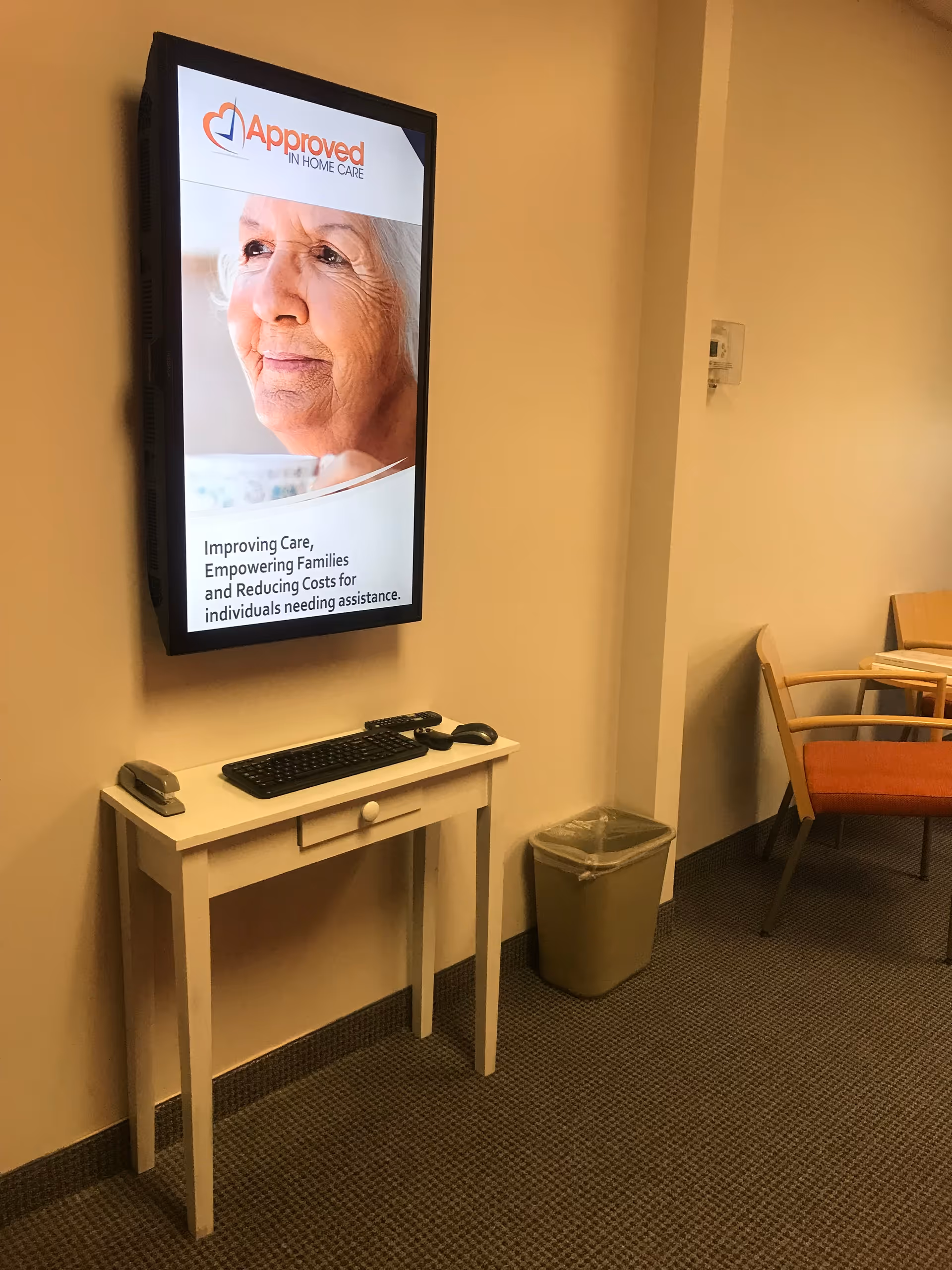 A hallway setup with a wall-mounted screen, desk, trash bin, and seating.