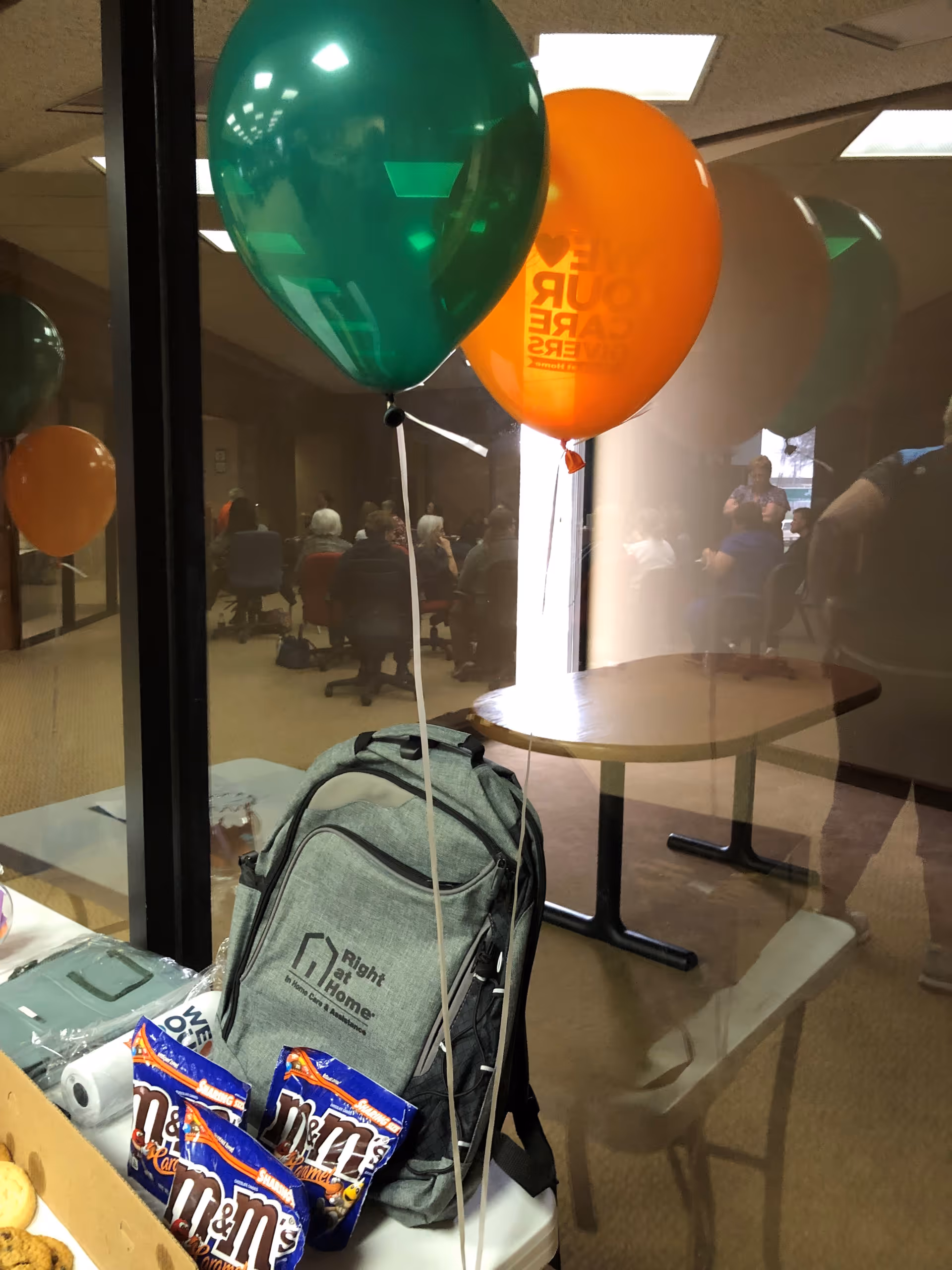 A backpack with balloons sits on a table in a senior living lobby.