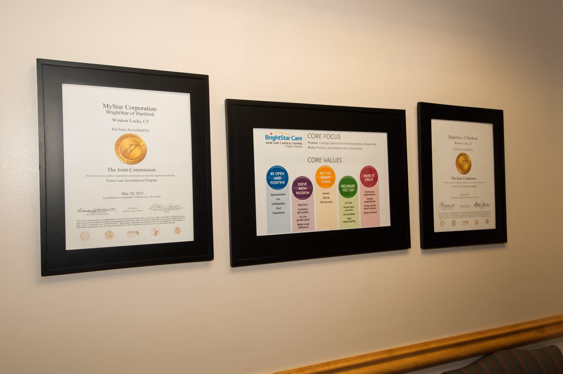 Three framed certificates hanging on a beige wall above a wooden trim.