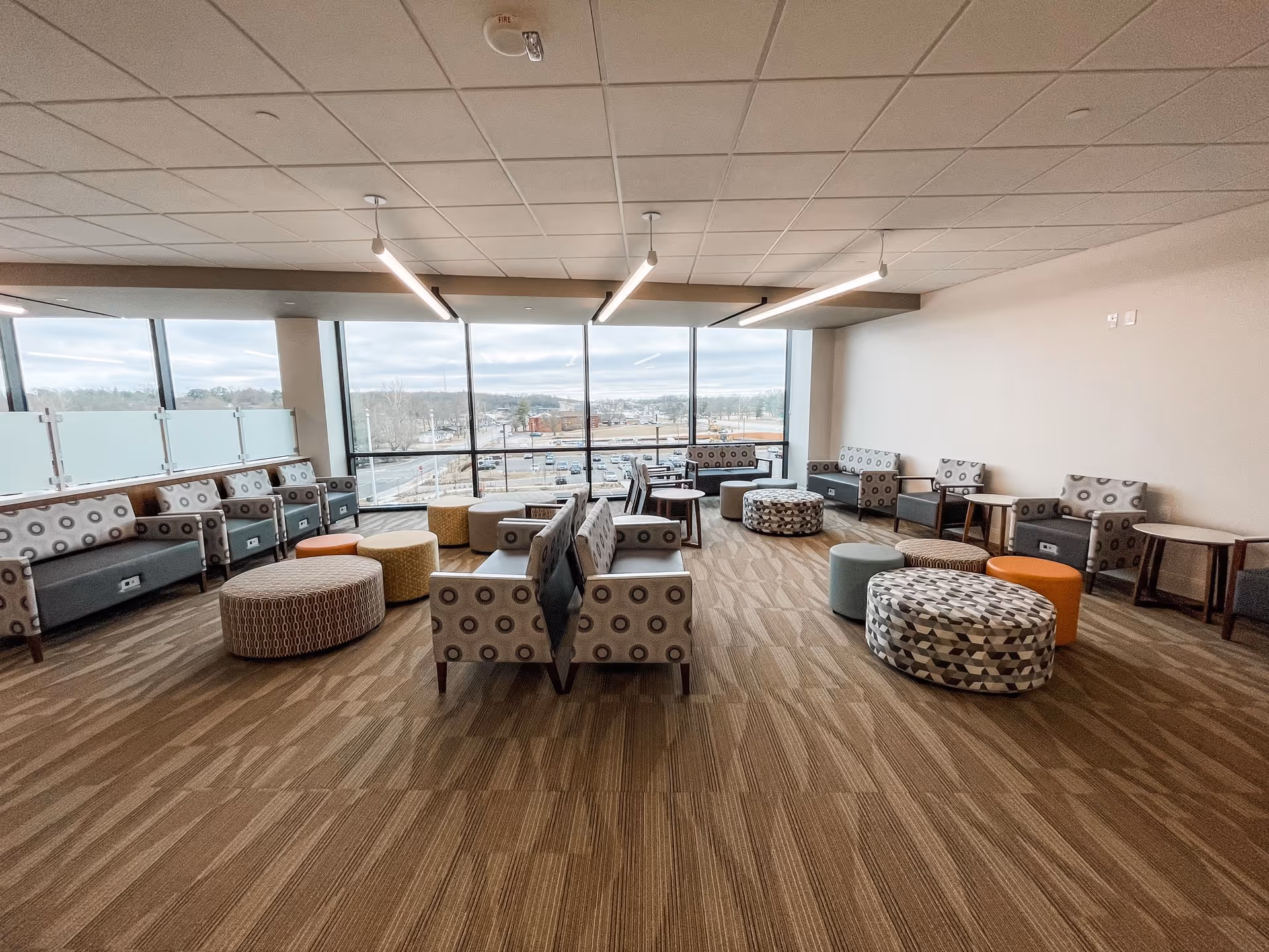 Spacious senior living lounge with patterned seating, ottomans, and large windows.