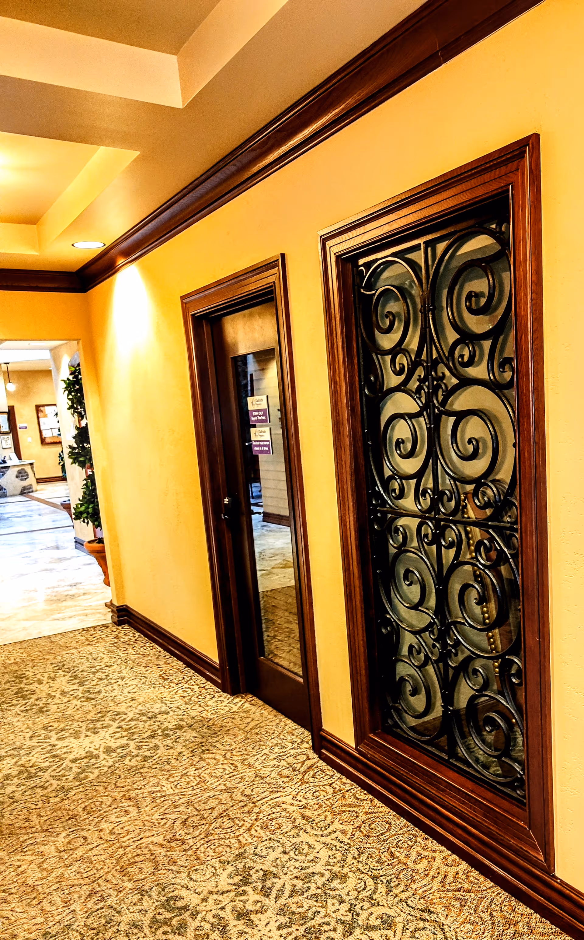 A warm yellow hallway with dark wood trim, carpet, and decorative iron window panels.
