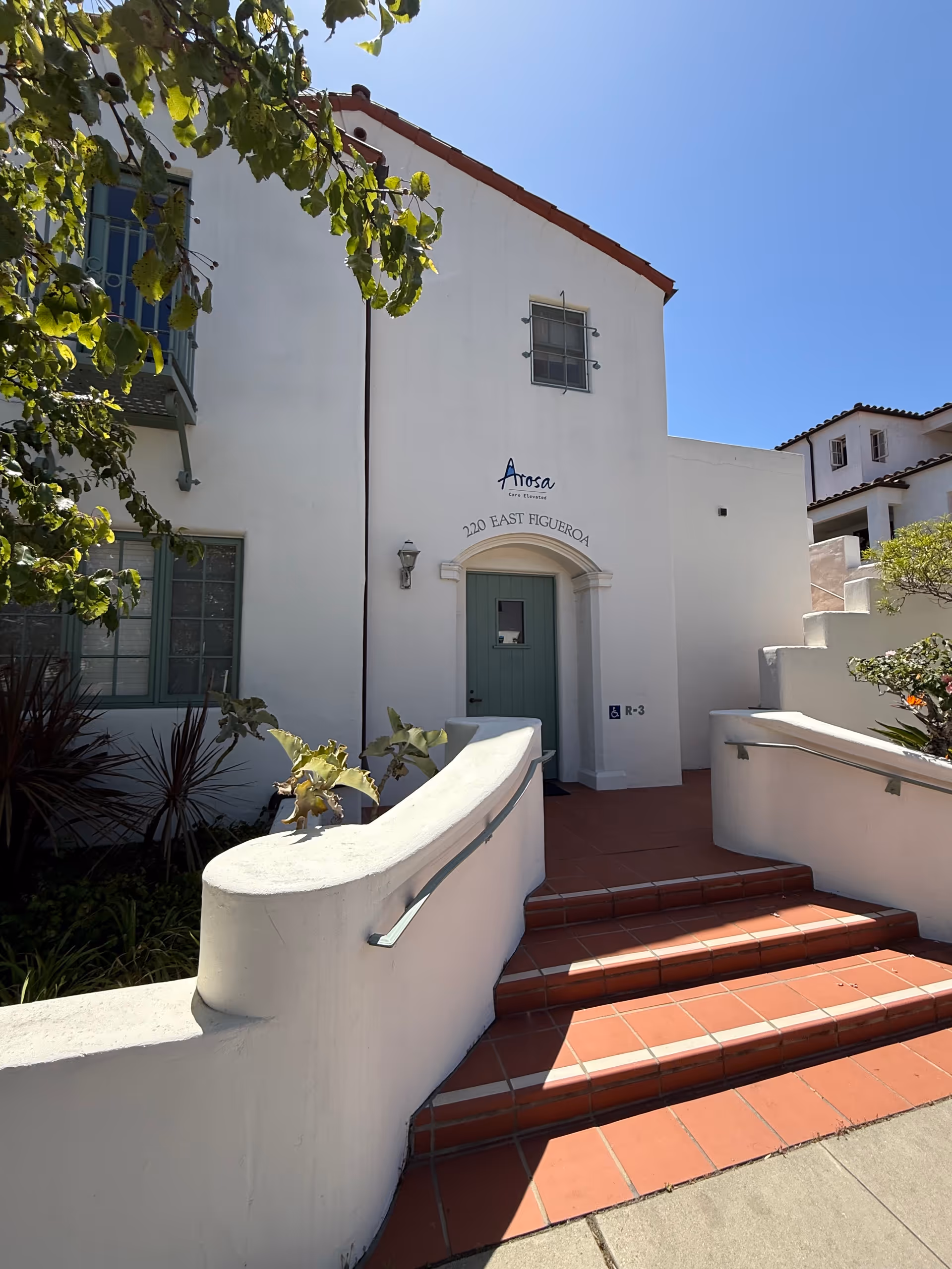 White stucco Arosa Central Coast exterior with teal door and red-tiled stairs.