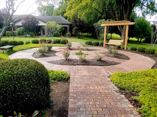 Circular brick-patio garden with a wooden swing and blooming rose bushes.