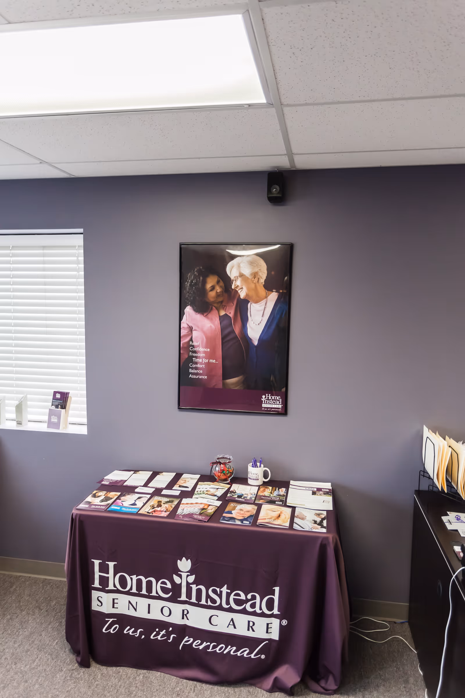 Purple-walled interior with a brochure table and Home Instead poster.