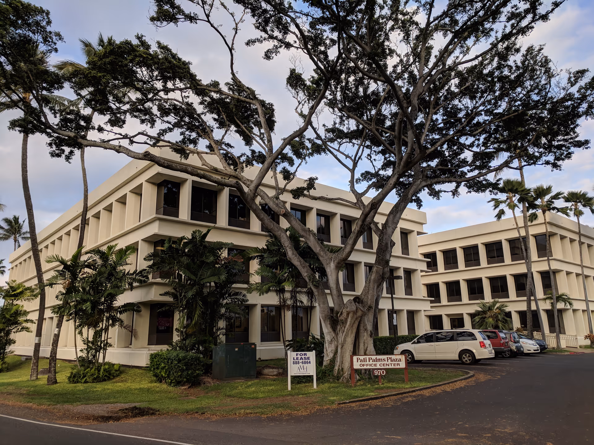 Beige multi-story senior living building with palm trees and parked cars in front.