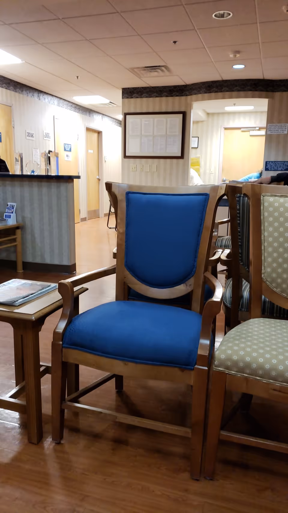 Interior waiting area with wooden chairs, blue cushions, and a reception desk.