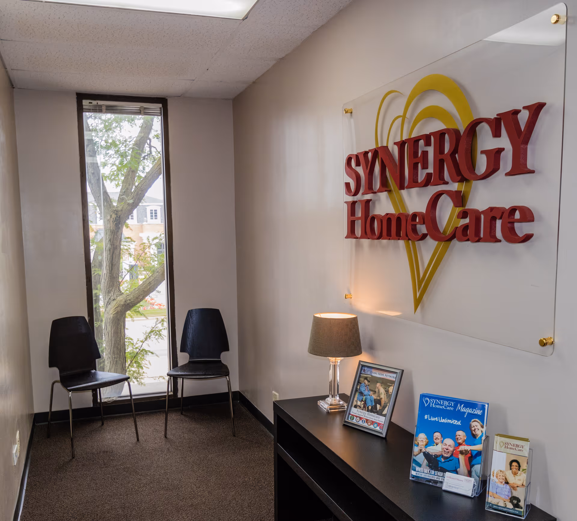 Reception area with a large SYNERGY HomeCare sign and two chairs.