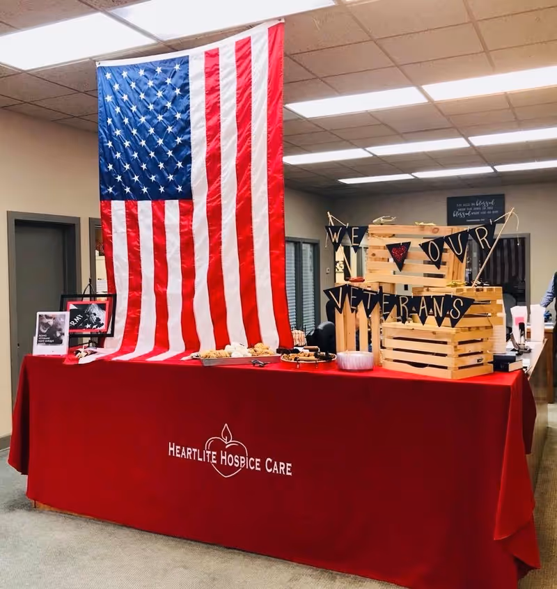 Indoor hospice display with a large American flag behind a red HeartLife table cover.