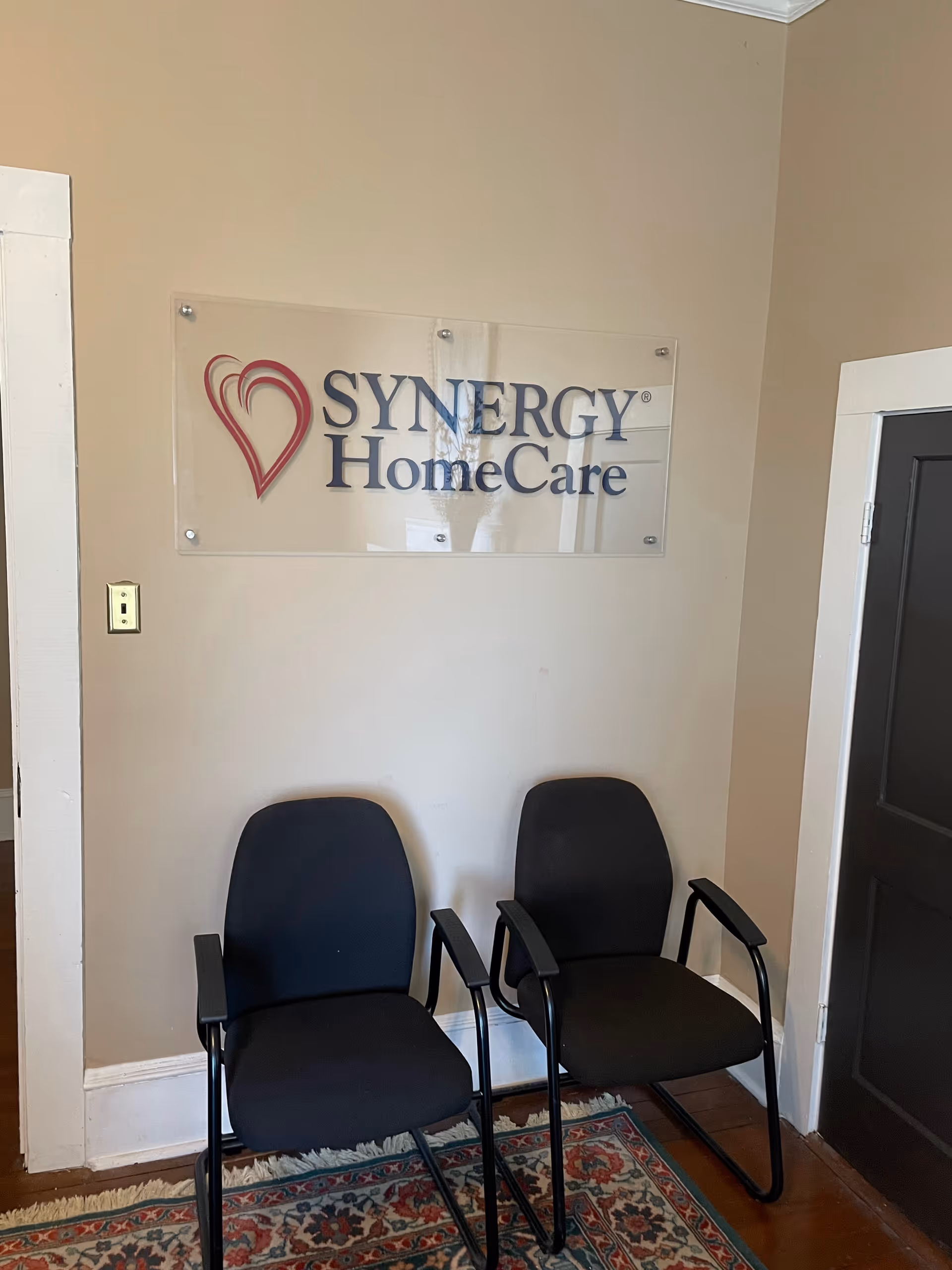 Two black chairs sit in a waiting area beneath a Synergy HomeCare sign.
