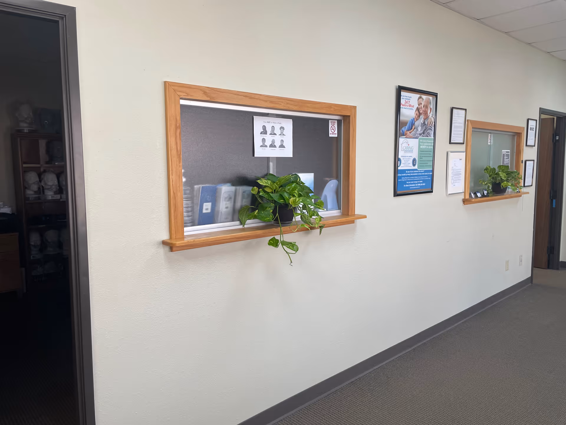 Interior hallway with two windowed service counters, posters, and potted plants.