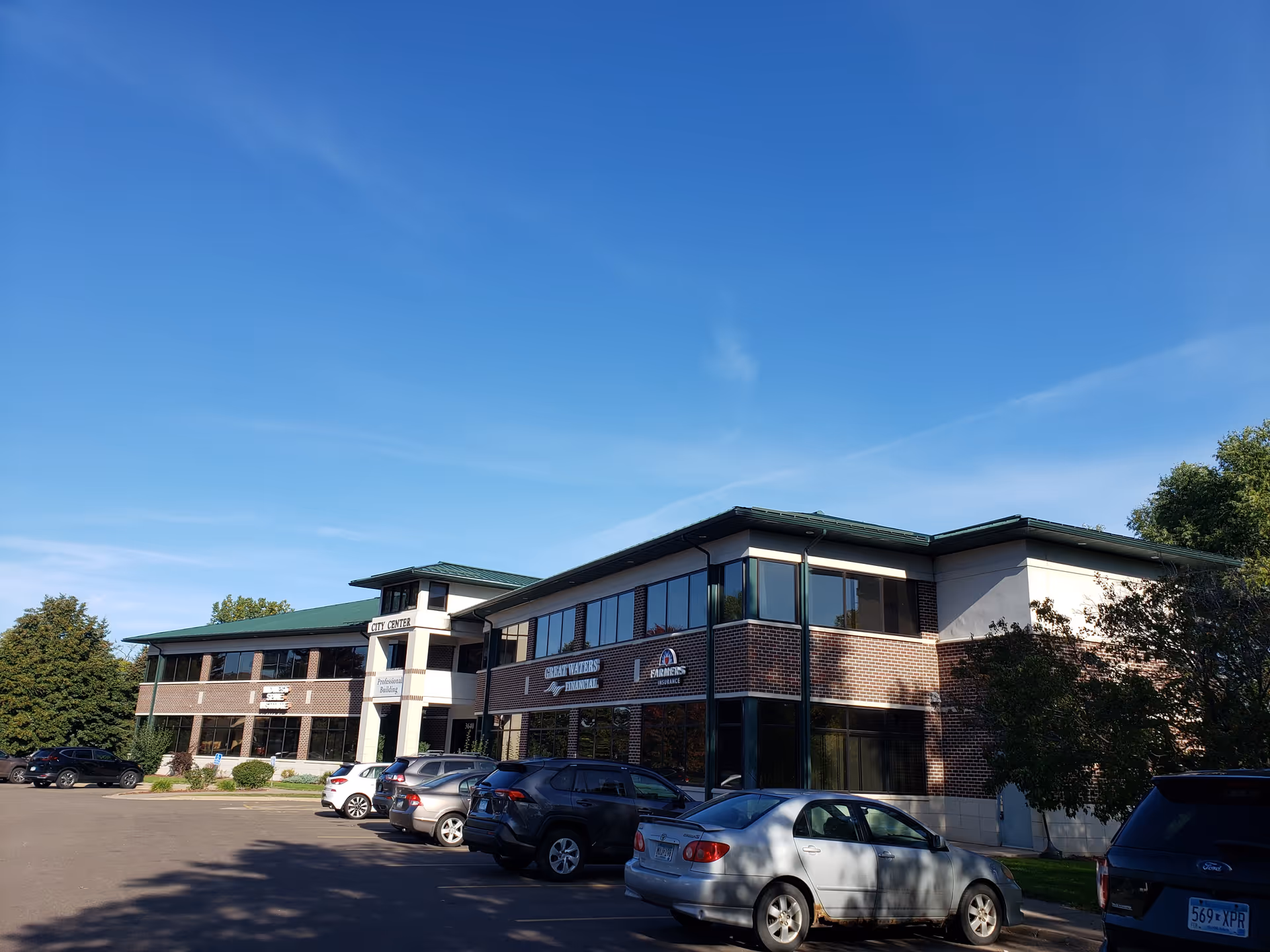 Exterior view of a two-story brick office building with parked cars under clear blue sky.