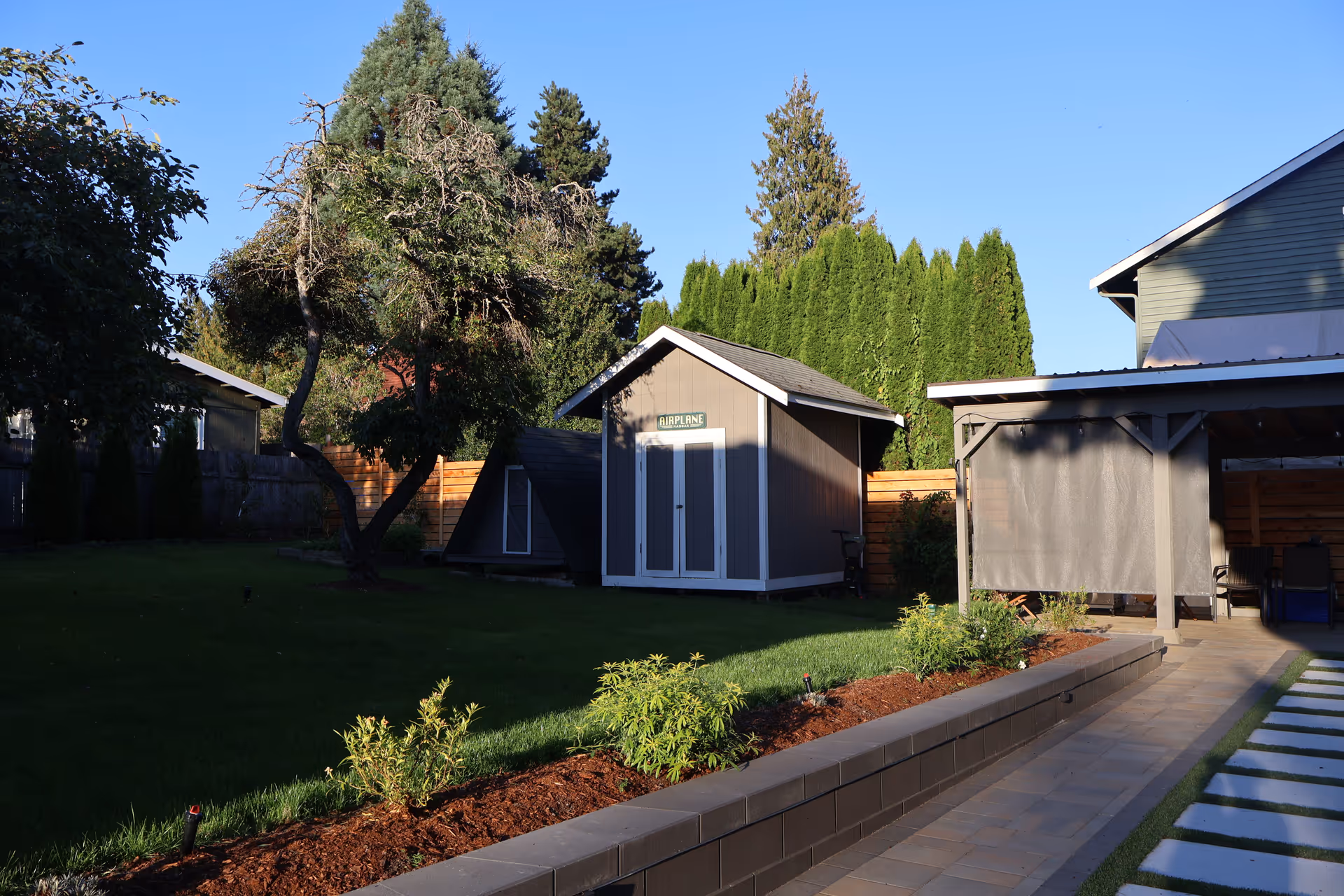 Well kept backyard with lawn, trees, a shed, and a covered patio.