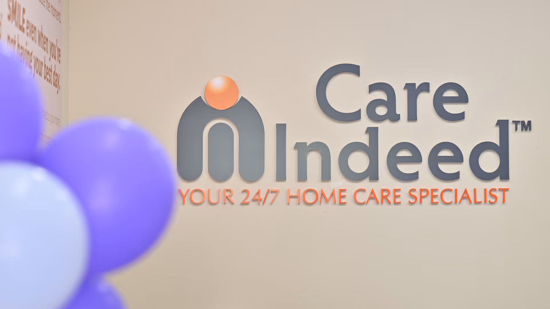 Interior wall displays the Care Indeed logo with purple balloons in a lobby.