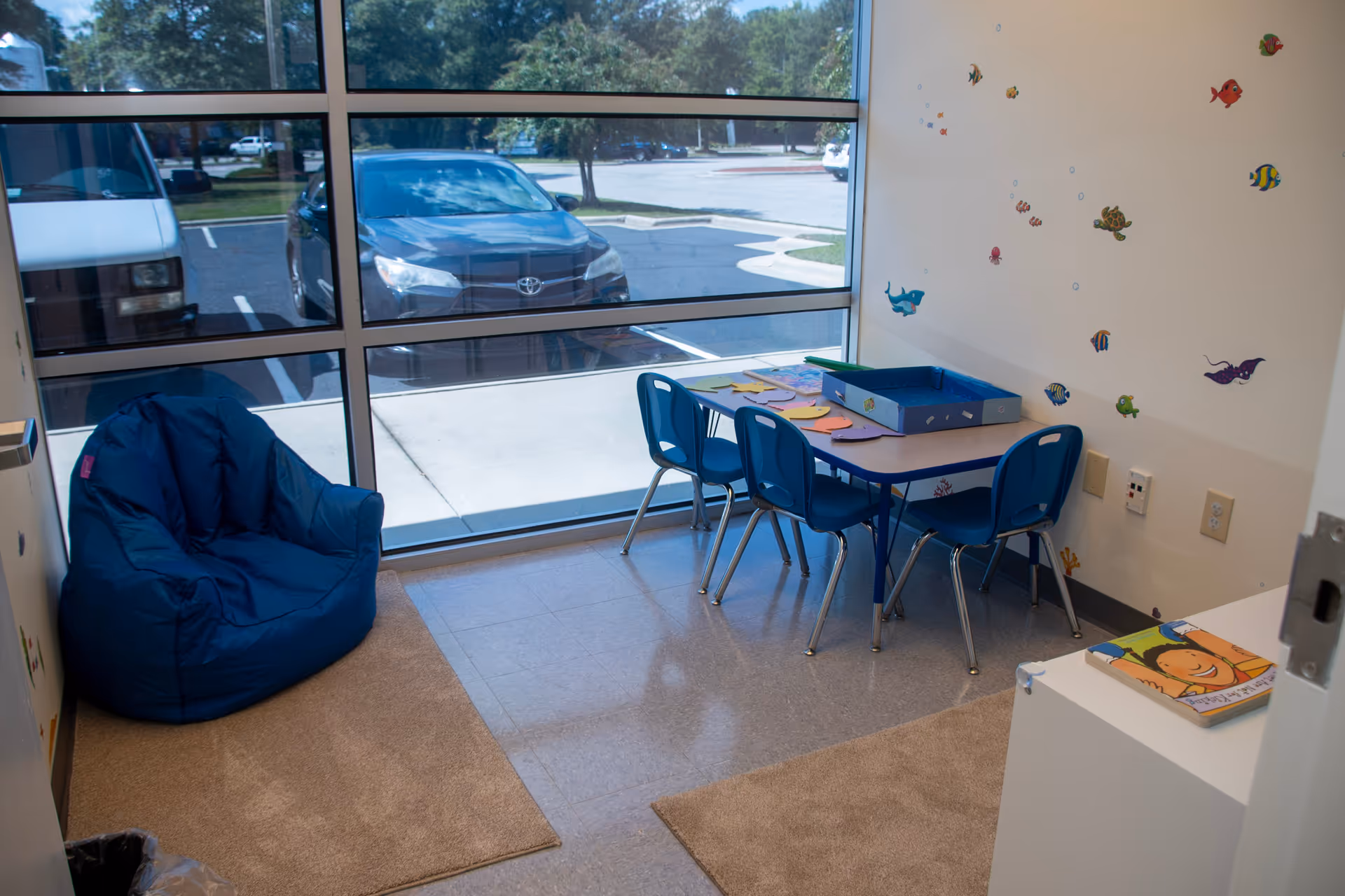 Bright indoor play area with blue bean bag, small table, chairs, and fish decals.