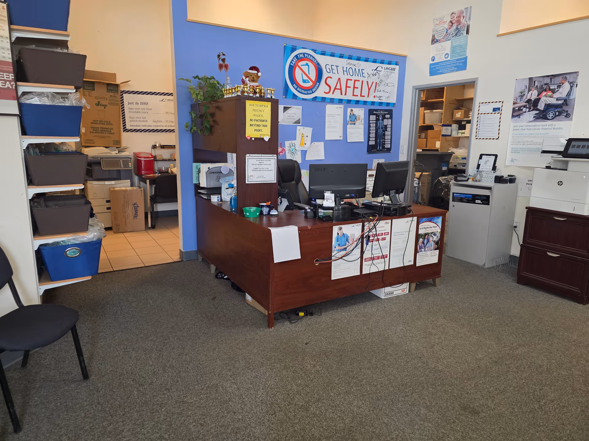 Reception desk with computers, posters, and storage shelves in a LINCARE facility lobby.