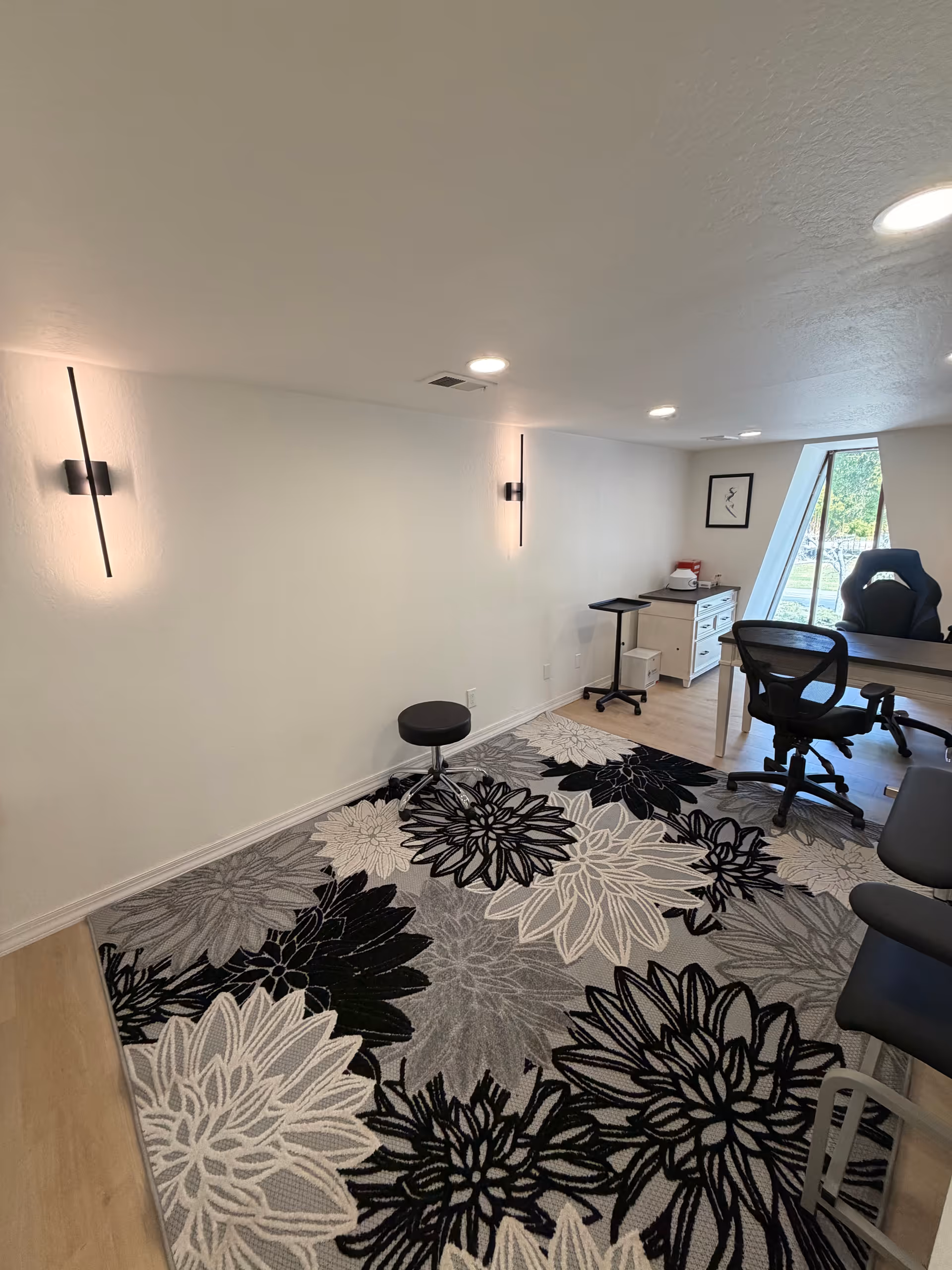 Small interior office space with floral rug, desk, chair, and window.