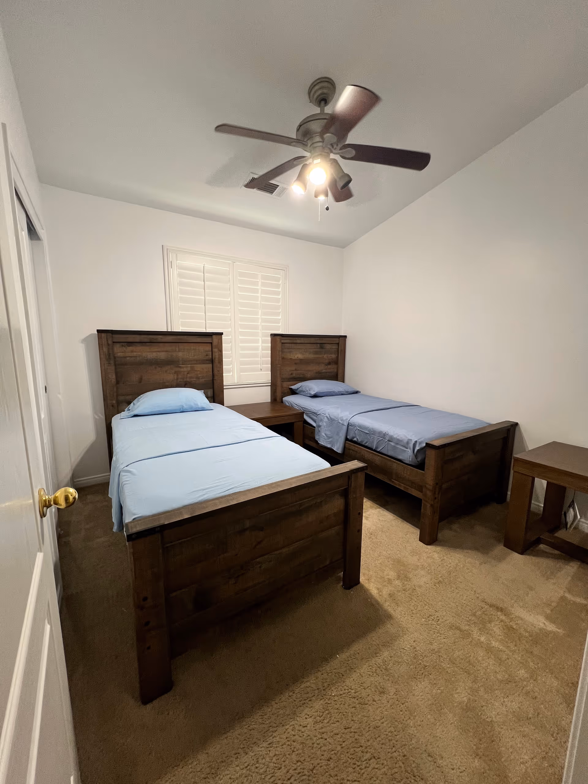 Two wooden twin beds with blue bedding, a ceiling fan, and a nightstand.