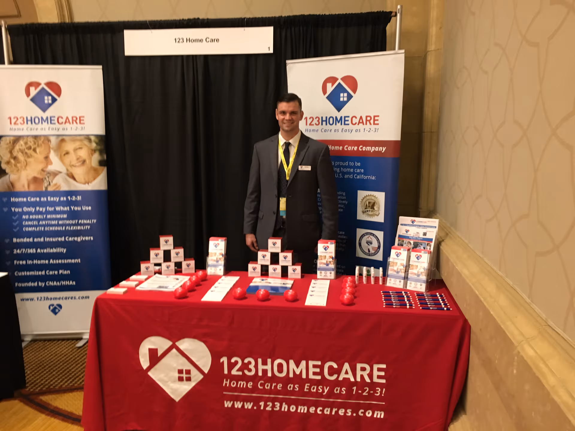 A man in a suit stands at a TheKey booth promoting elder care services.