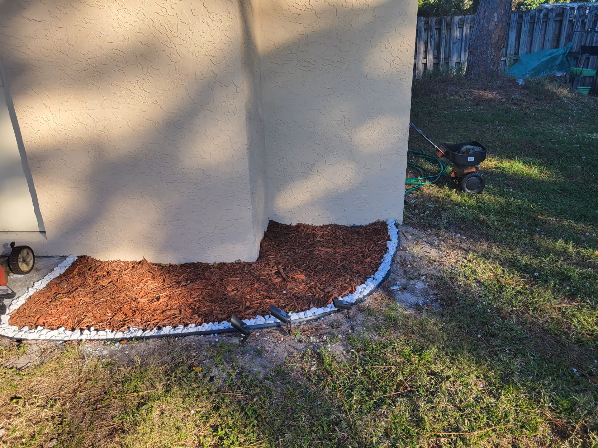 Exterior corner of building with mulch bed bordered by white stones.
