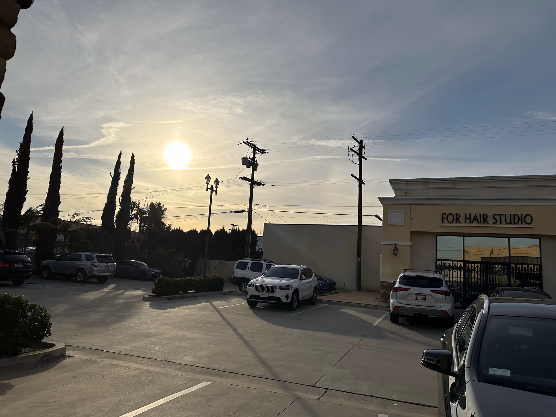 Sunlit parking lot in front of a beige building labeled For Hair Studio.